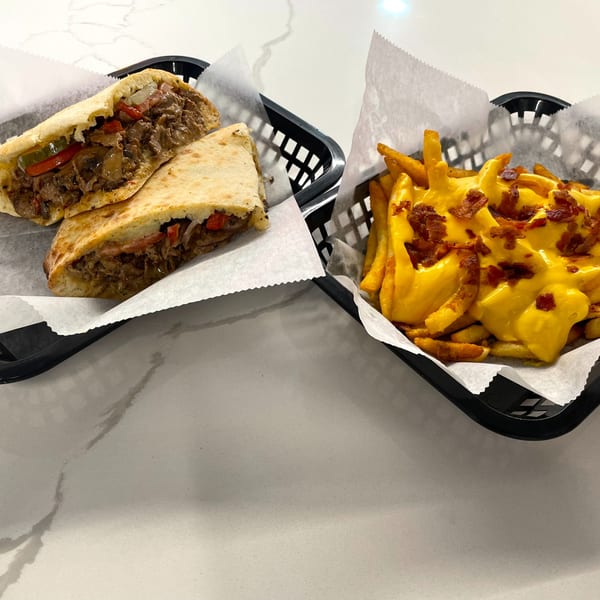 Two baskets of food: a cheesesteak quesadilla and cheese fries with bacon bits.