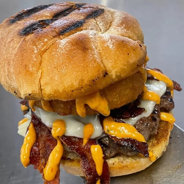 A juicy burger with bacon, melted cheese, onion rings, and a creamy orange sauce on a grilled bun.