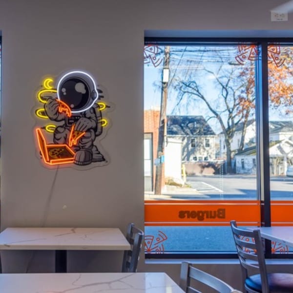 Neon astronaut eating pizza at Johnny's Pockets, with tables and a window view of the street.