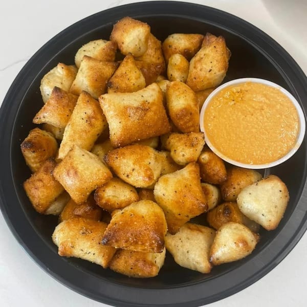 Golden-brown Johnny's Pockets pizza bites with seasoning, served in a black bowl with a side of dipping sauce.
