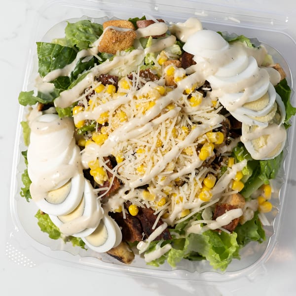 A Caesar salad with lettuce, corn, croutons, parmesan cheese, hard-boiled eggs, and dressing.