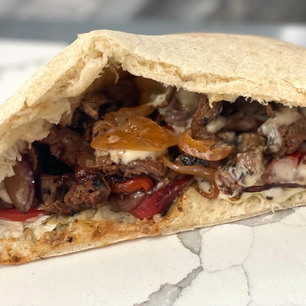 A Johnny's Pockets pita sandwich, filled with steak, caramelized onions, red peppers, and melted cheese.