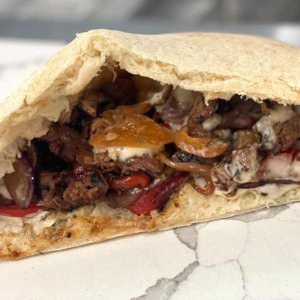 A Johnny's Pockets pita sandwich, filled with steak, caramelized onions, red peppers, and melted cheese.