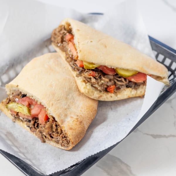 Two Johnny's Pockets sandwiches with meat, tomatoes, and pickles in a black basket.