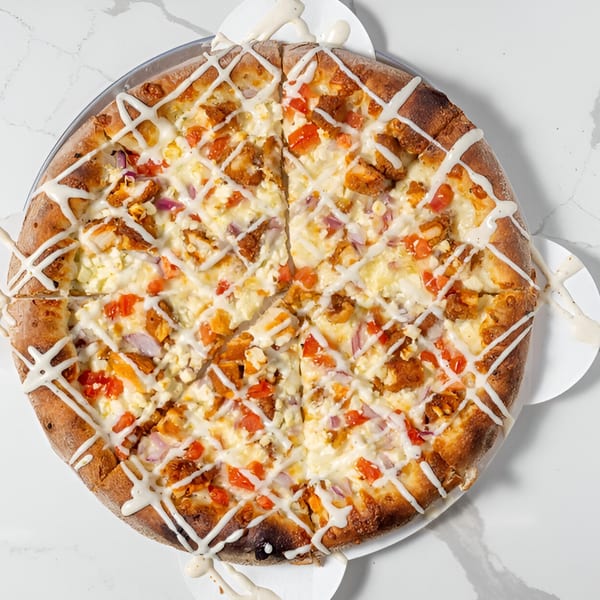 A Johnny's Pockets pizza, topped with chicken, tomatoes, onions, feta, and a white sauce drizzle.