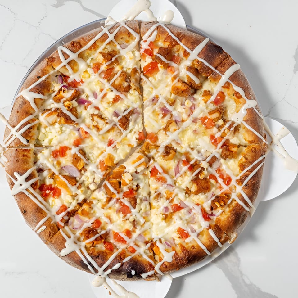 A Johnny's Pockets pizza, topped with chicken, tomatoes, onions, feta, and a white sauce drizzle.