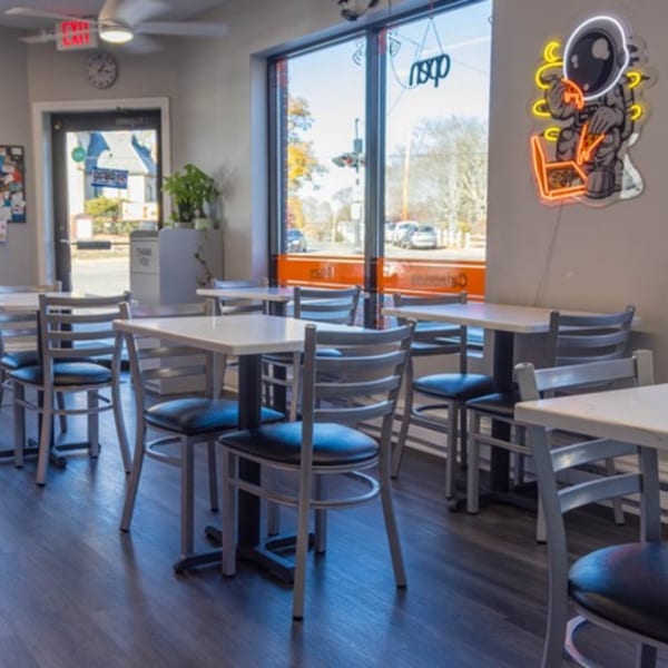 Interior of Johnny's Pockets with tables, chairs, and a neon astronaut eating pizza on the wall.