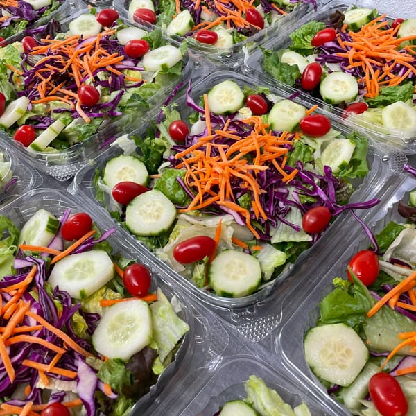 Multiple plastic containers of fresh Johnny's Pockets salads with lettuce, cucumbers, tomatoes, carrots, and cabbage.